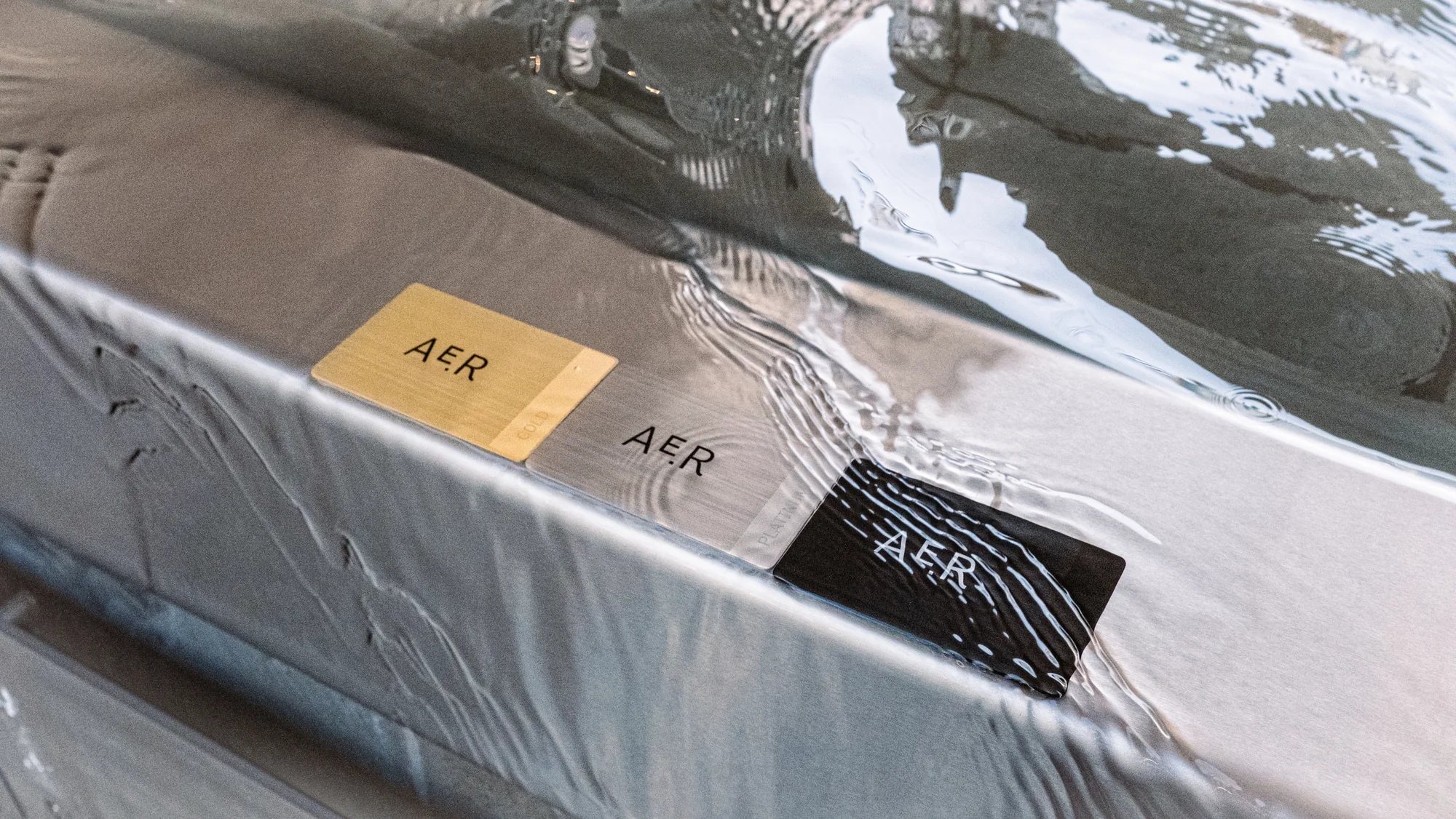 AE.R Gold, Platinum and Noir membership cards on wet marble as water runs across them